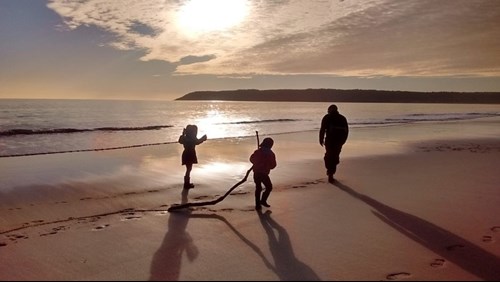 Teulu yn chwarae ar y traeth ar fachlud haul ym Mae Tor, Gŵyr